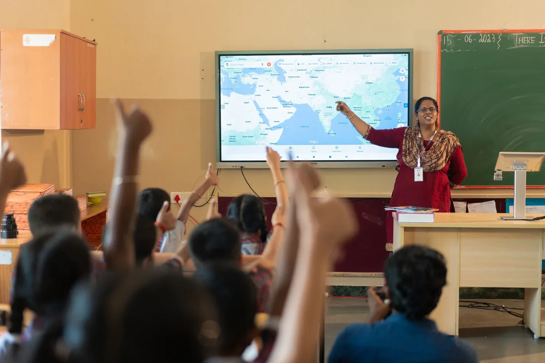 A teacher using Genie on the classroom screen while students raise their hands